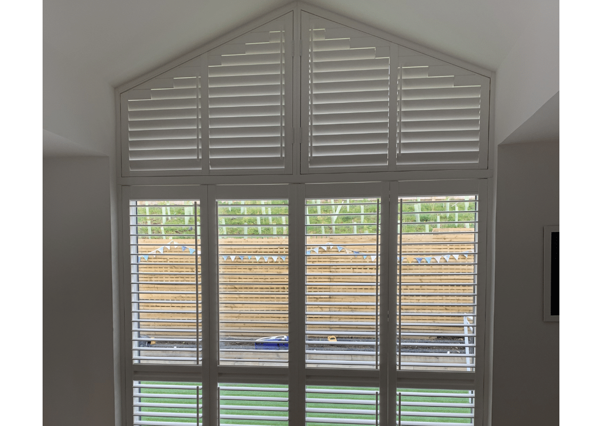 White tier-on-tier shutters installed on large gable windows in a modern Glasgow home with custom shaped shutter panels and privacy louvres.