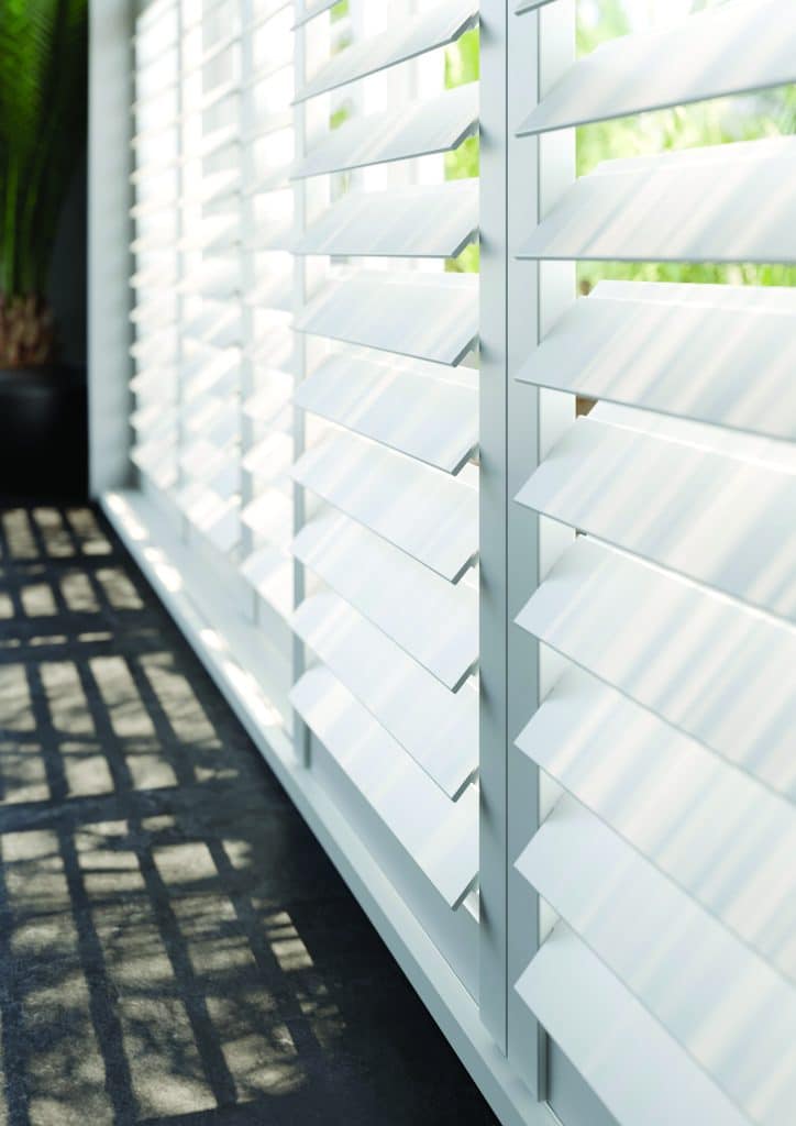 White plantation shutters with larger 76mm louvres allowing natural light to filter through large modern windows.