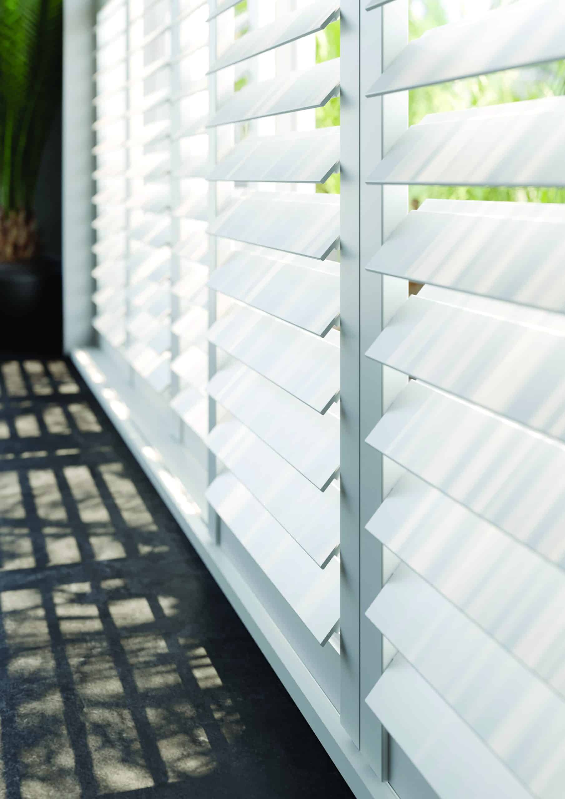 White plantation shutters with larger 76mm louvres allowing natural light to filter through large modern windows.
